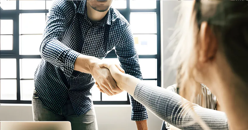 Two people shaking hands in a bright office.